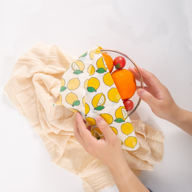 Reusable produce bag with fruit pattern held by hands on a white background