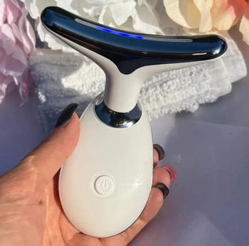 Hand holding a white electronic device with a black handle, possibly a cleaning tool, against a blurred background.